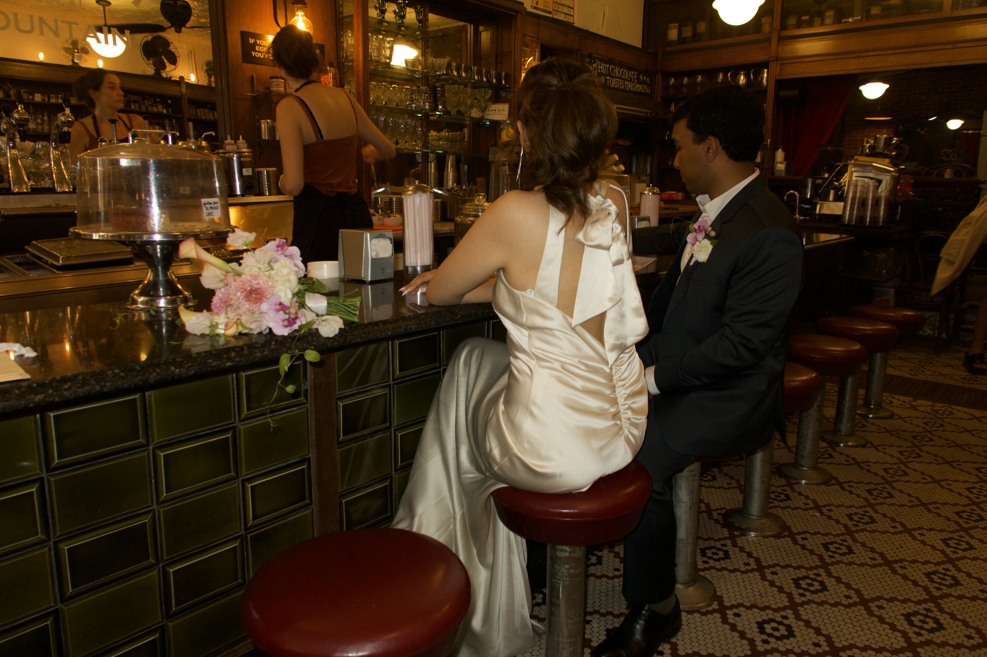Zarnab at the bar, seen from behind, in a satin dress